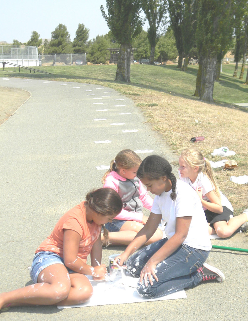 GIRL SCOUTS paint paw prints to lead to the dog park section of Community Park. Donna Beth Weilenman/ Staff