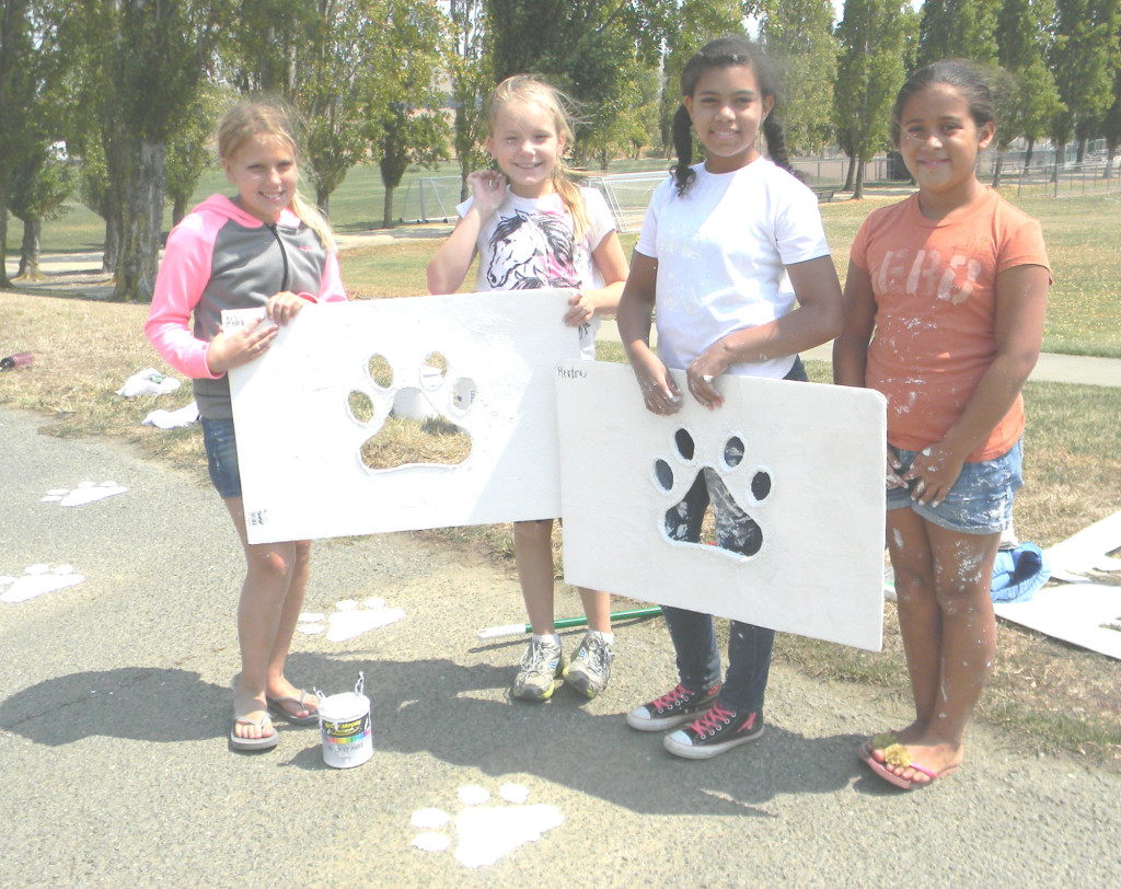 GIRL SCOUTS (from left) Katie Edwards, Kailey Magel, Sarah Jennings and Meadow Iniguez hold stencils used to paint paw prints on the walkway at Community Park. Donna Beth Weilenman/Staff